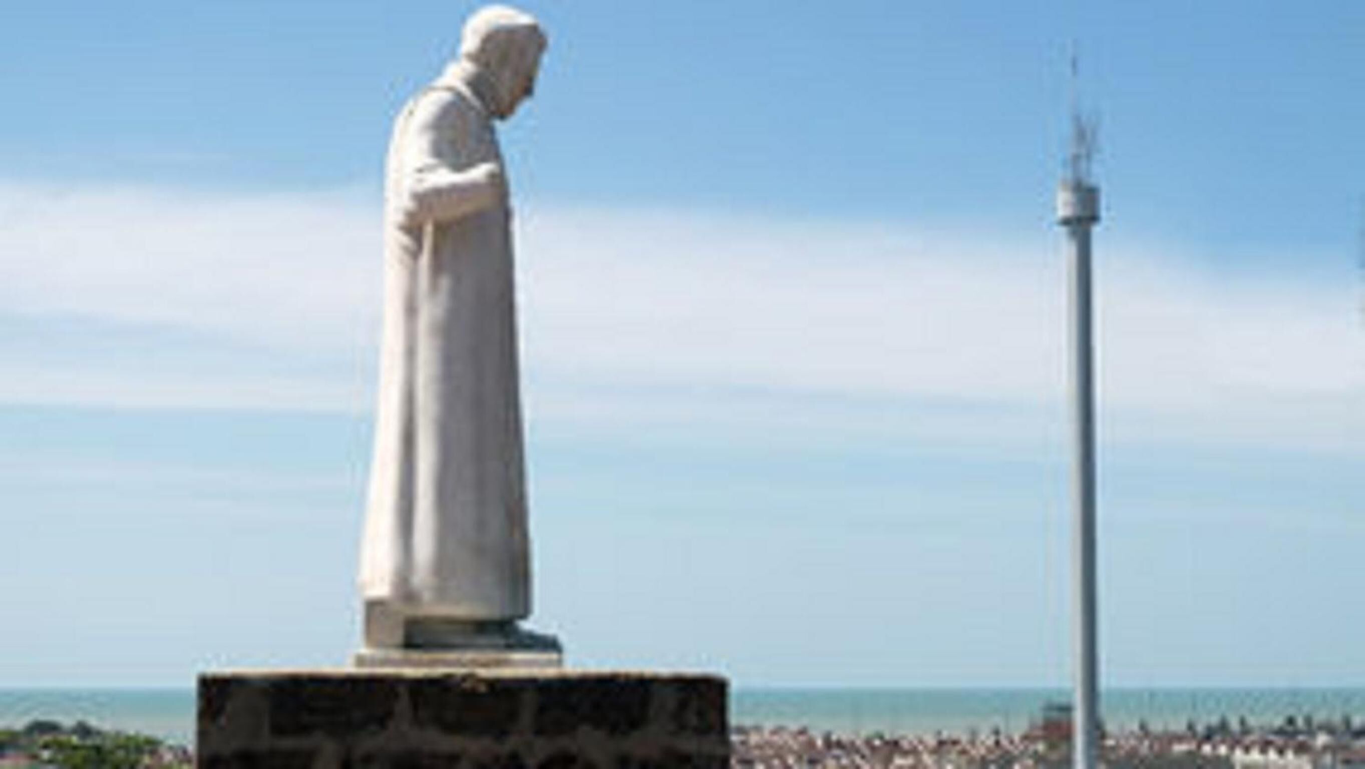 A statue on a pedestal with a clear sky and a body of water in the background.