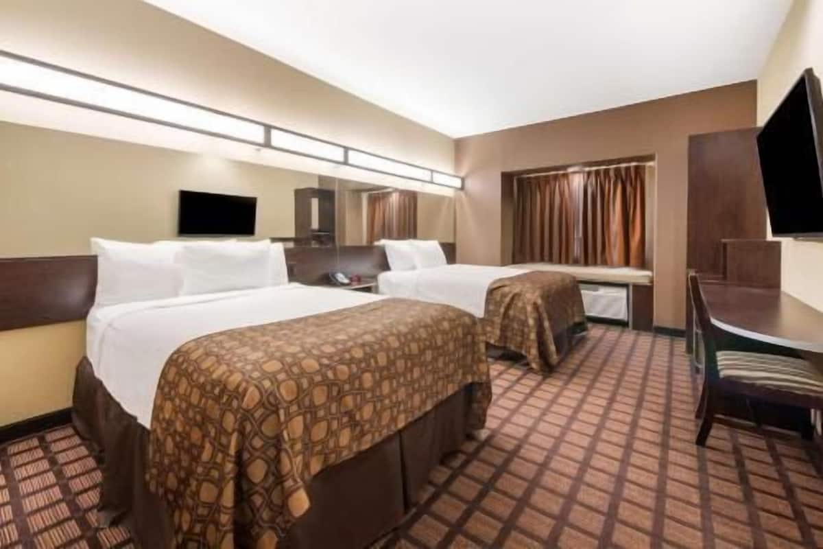 A hotel room with two beds, a desk, a television, and a mirror.