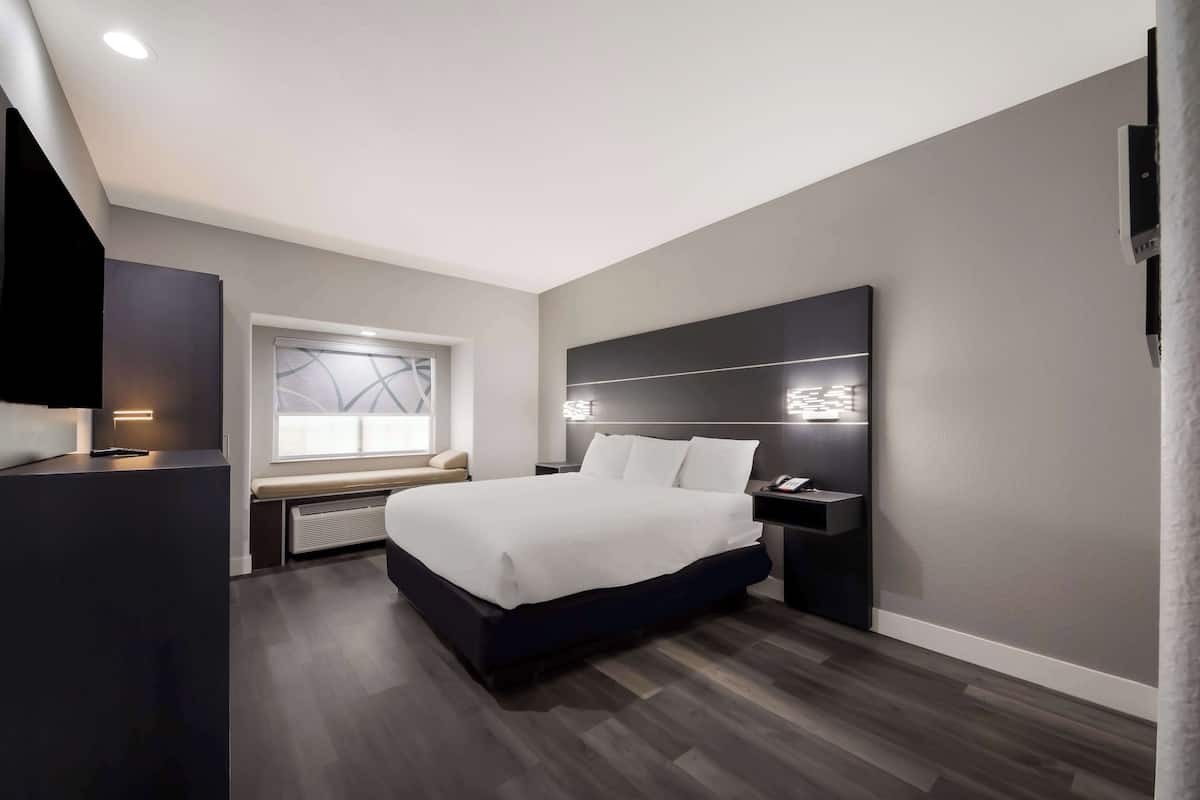 A modern bedroom with a large bed, bedside tables, a built-in bench, and a window with a view.