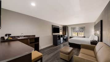 A hotel room with a kitchenette, a bed, a sofa, and a TV.