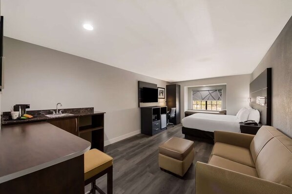 Habitación de hotel con kitchenette, cama, sofá y televisor.