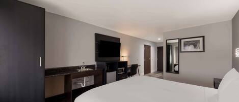 Una habitación de hotel moderna con una cama grande, un televisor de pantalla plana, un escritorio con una silla, un espejo y un armario.