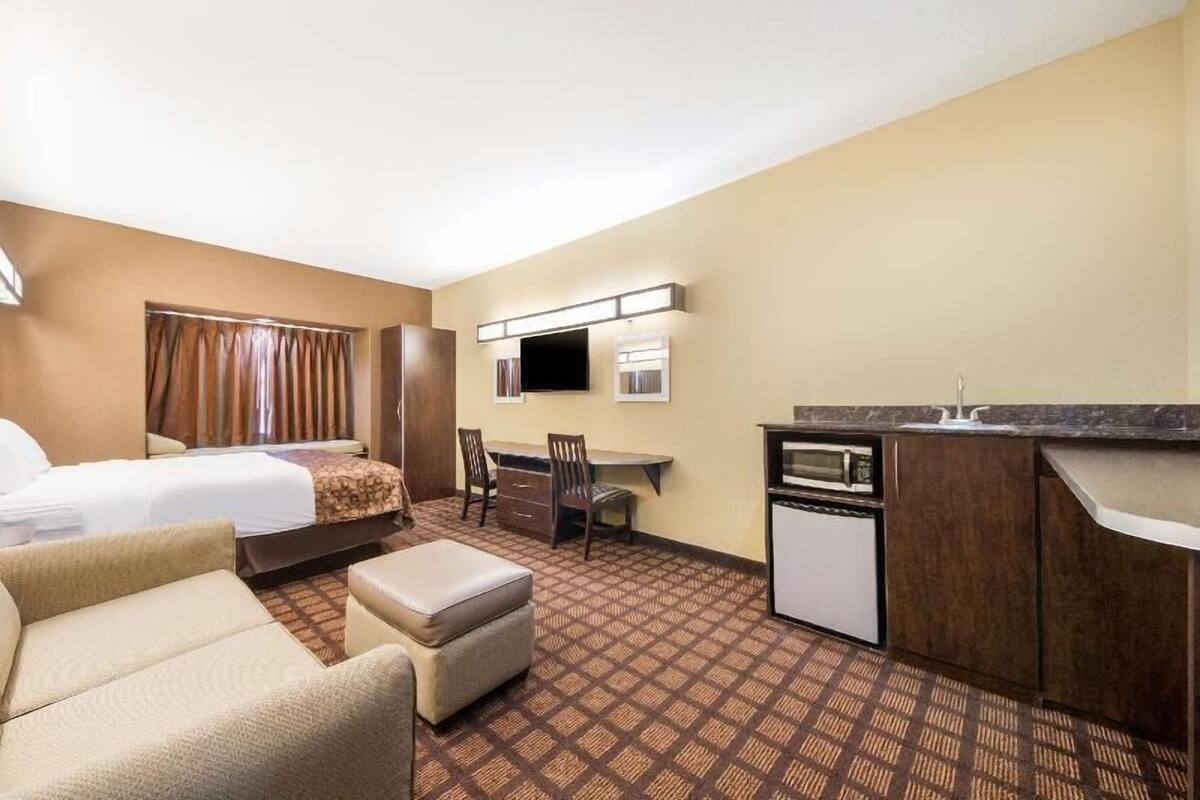 A hotel room with a bed, a desk, a chair, a microwave, and a small kitchenette.