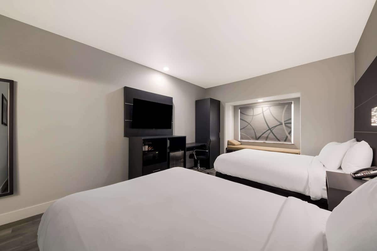A modern hotel room with two beds, a desk, a flat-screen TV, and a window with a decorative view.