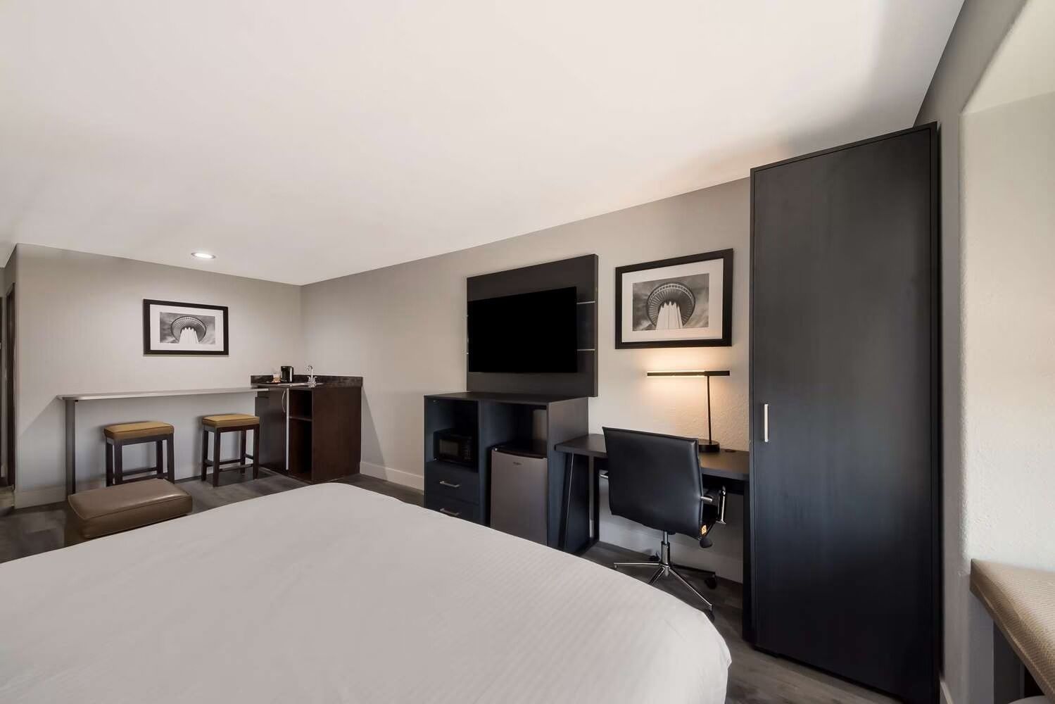 A hotel room with a large bed, a desk with a chair, a television, and two framed pictures on the wall.