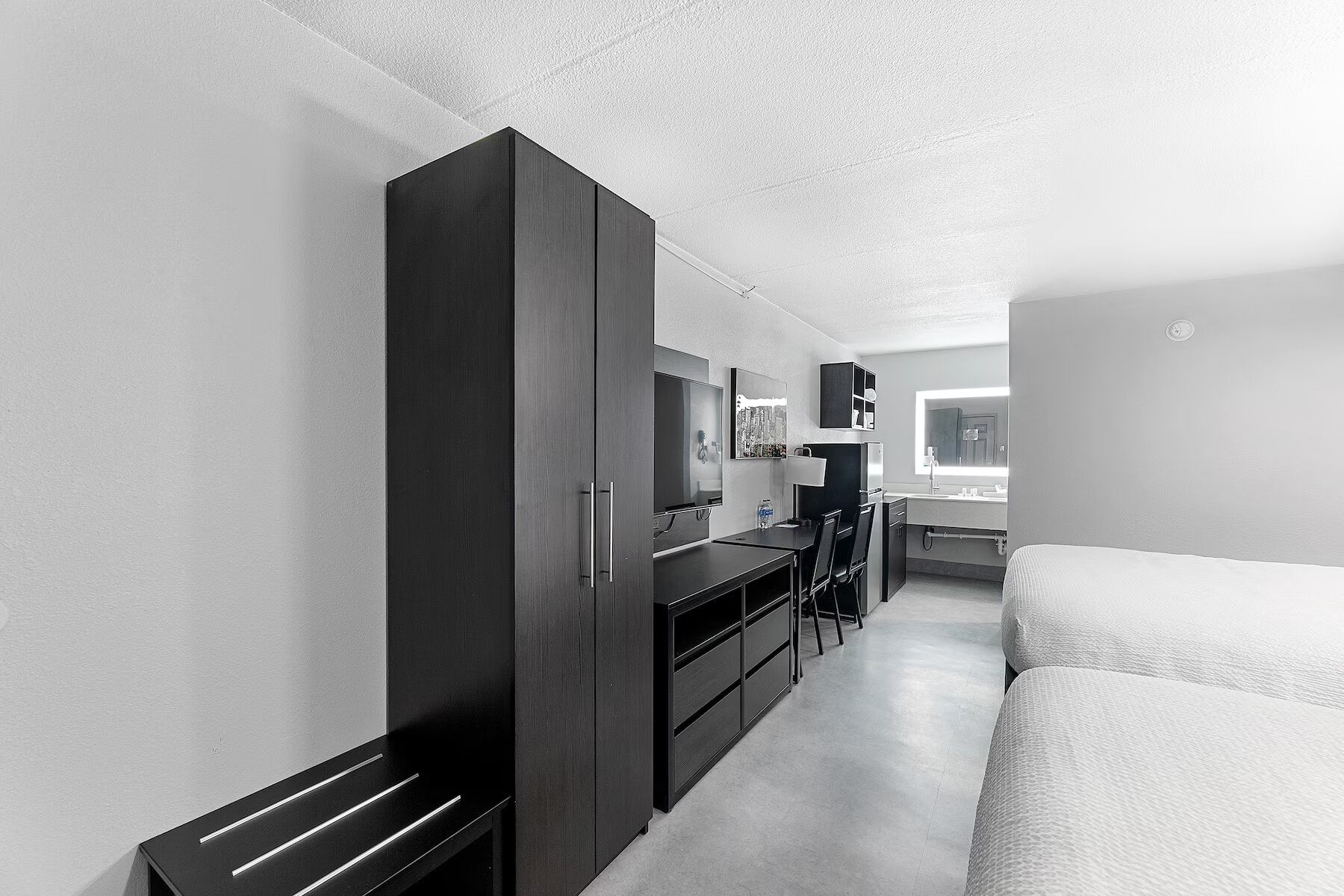 Een kleine hotelkamer met een bed, bureau, kledingkast en spiegel.