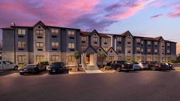 A multi-story hotel with a stone facade, a central entrance, and a parking lot with several cars. - Best Western SeaWorld San Antonio (San Antonio)