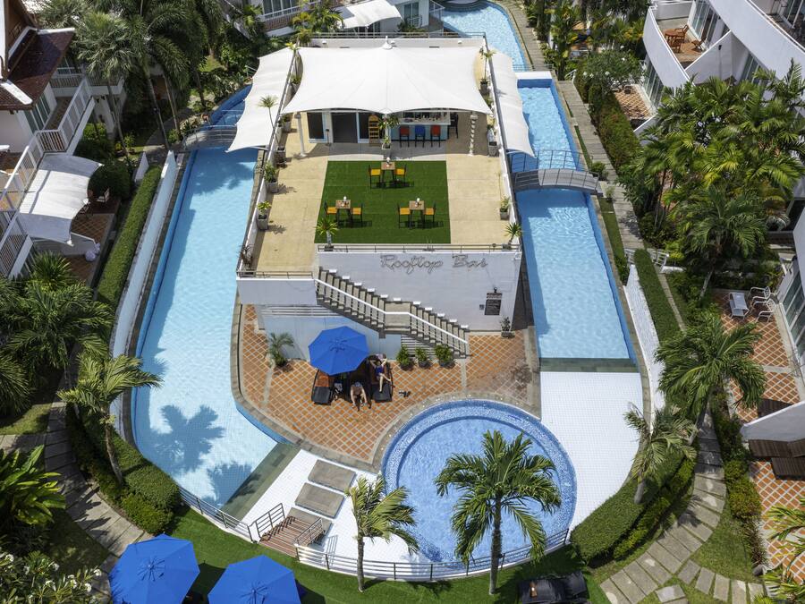 Un área de piscina en la azotea con bar, asientos y palmeras.