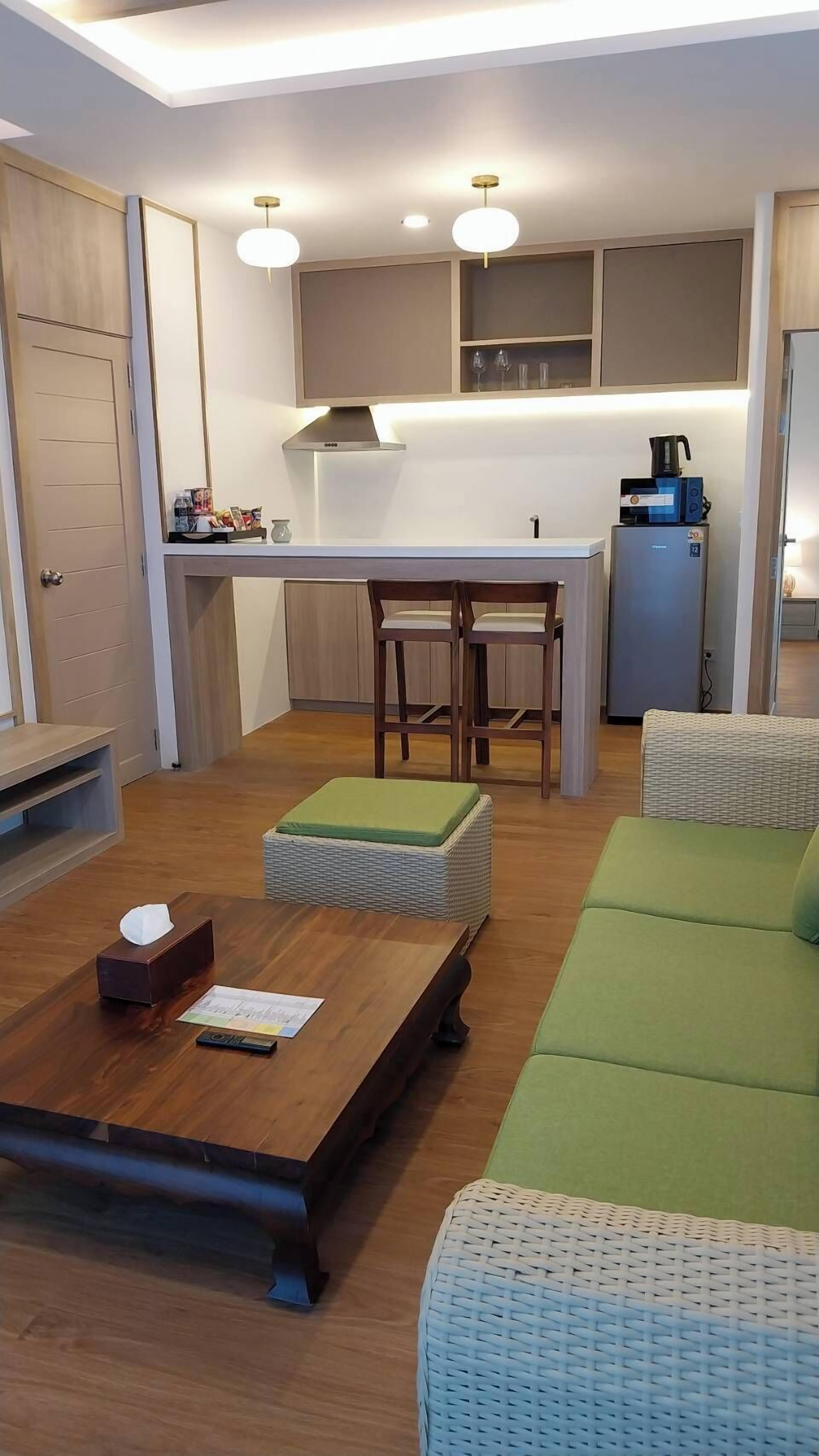 A compact living space with a kitchenette, a wooden dining table, a green sofa, and a wicker ottoman.