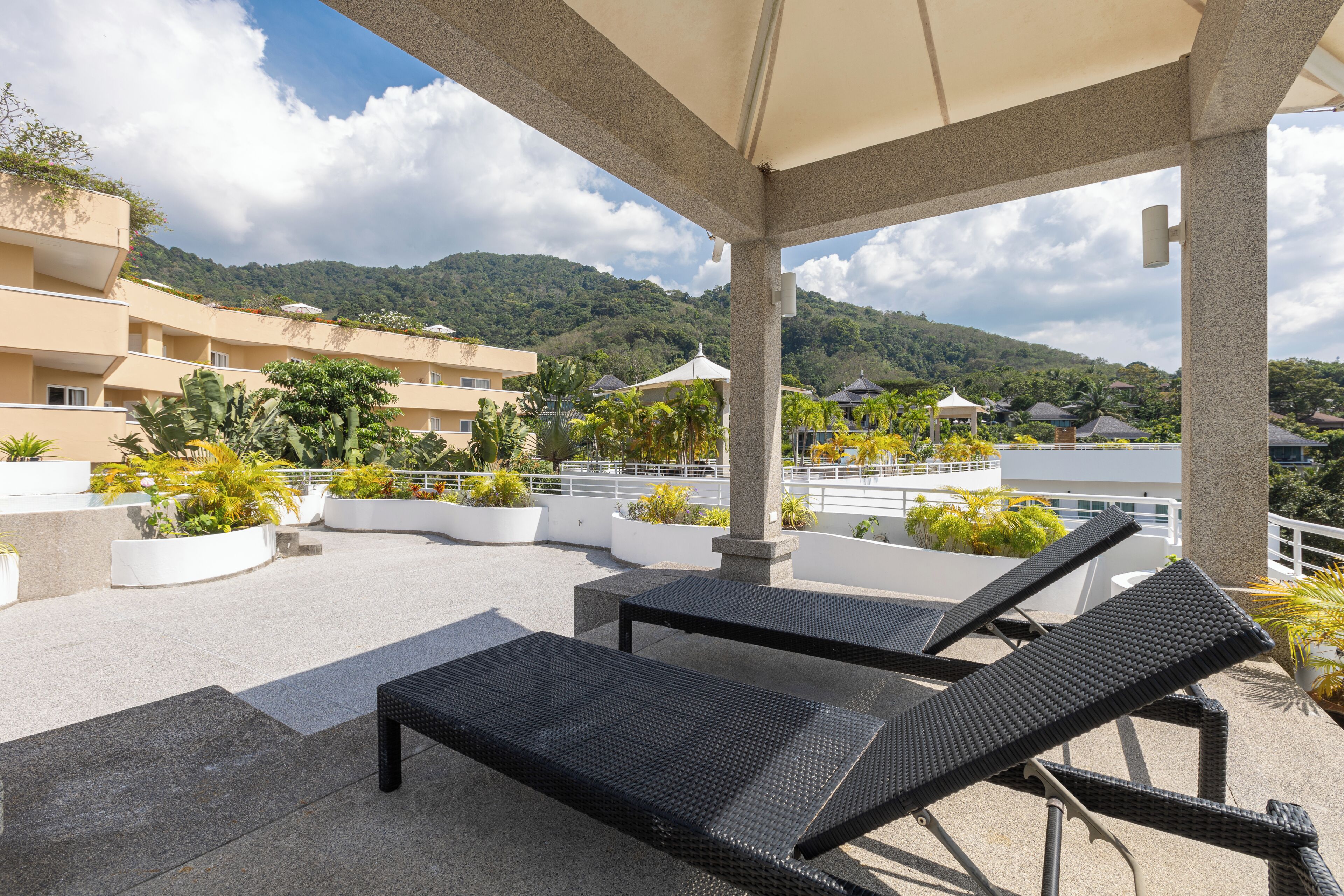 Una terraza en la azotea con sillones de descanso, plantas en macetas y vistas a un paisaje montañoso.