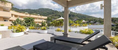 Una terraza en la azotea con sillones de descanso, plantas en macetas y vistas a un paisaje montañoso.