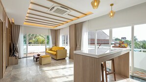 A spacious living area with a large window, a sofa, a coffee table, and a kitchen island. - Phunawa Resort Karon Beach Phuket (Karon)