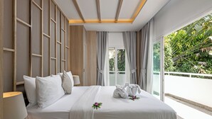 A hotel room with a large bed, a nightstand, a lamp, and a view of greenery outside. - Phunawa Resort Karon Beach Phuket (Karon)