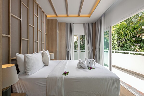 A hotel room with a large bed, a nightstand, a lamp, and a view of greenery outside. - Phunawa Resort Karon Beach Phuket (Karon)
