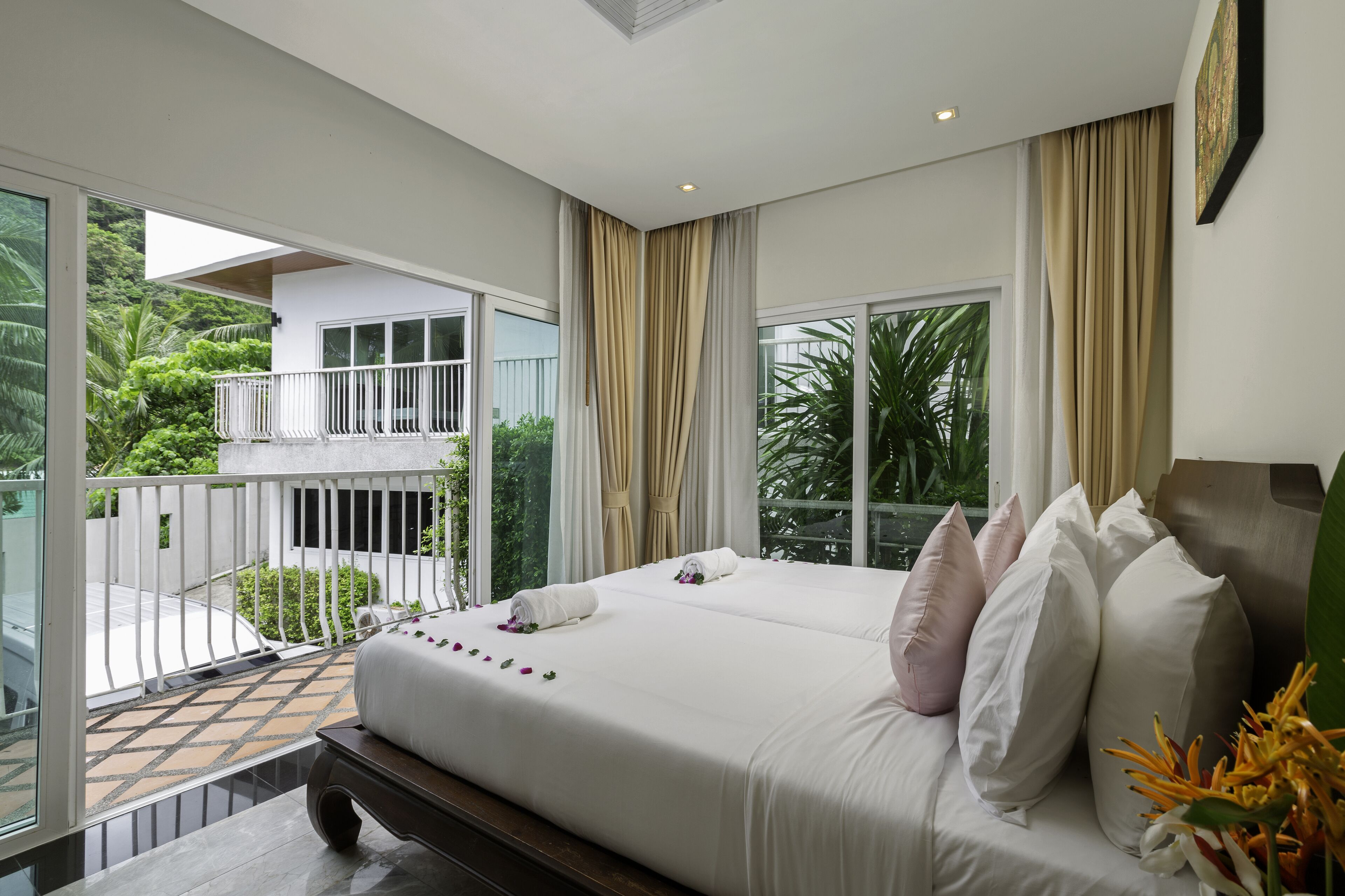 A hotel room with a large bed, a balcony with a view of greenery, and a window with curtains.