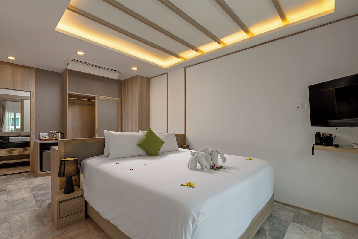 A modern hotel room with a large bed, bedside table, lamp, and a TV mounted on the wall.
