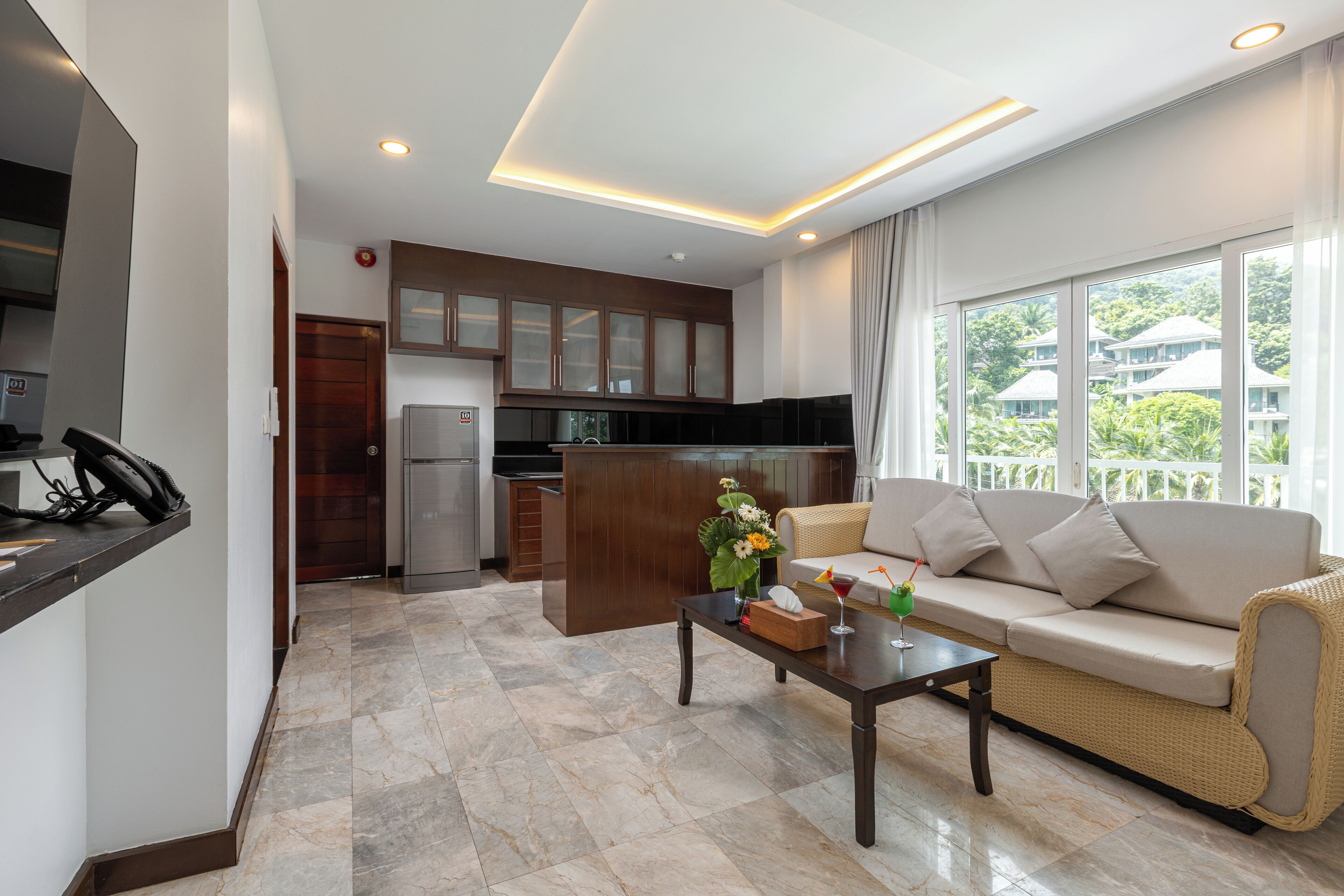 A modern living room with a sofa, a coffee table, and a kitchen area with cabinets and a refrigerator.