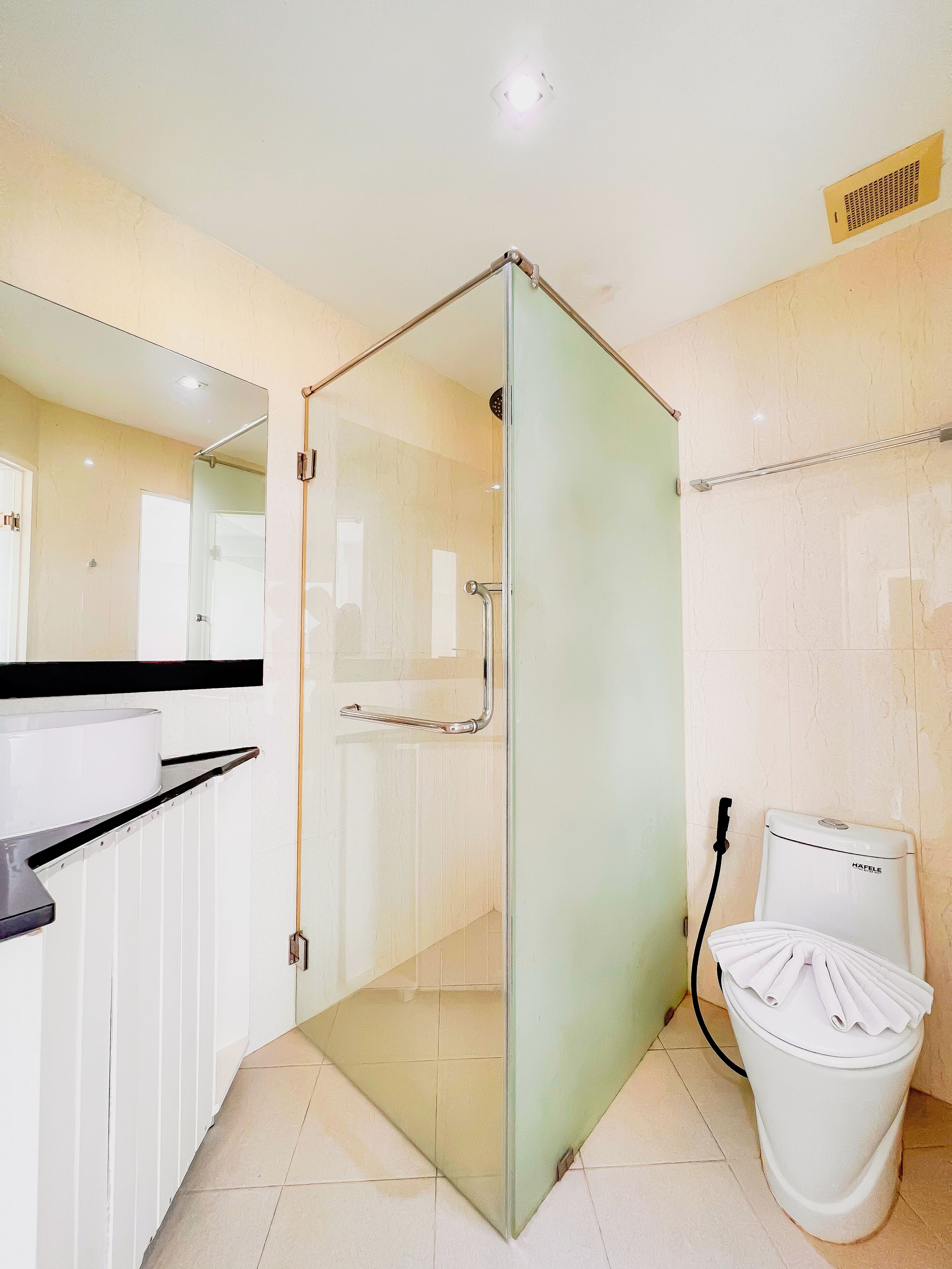 A bathroom with a glass-enclosed shower, a toilet, and a sink with a towel rack.