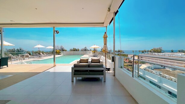 A rooftop pool area with lounge chairs and umbrellas, a seating area with cushions, and a view of the sea. - Grand Sunset Hotel Phuket (Karon)