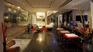 A modern hotel lobby with a glass wall, a seating area with sofas, a reception desk, and a computer station. - Grand Sunset Hotel Phuket (Karon)