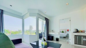 A modern hotel room with a glass dining table, a sofa, a bed, and a kitchen area. - Grand Sunset Hotel Phuket (Karon)