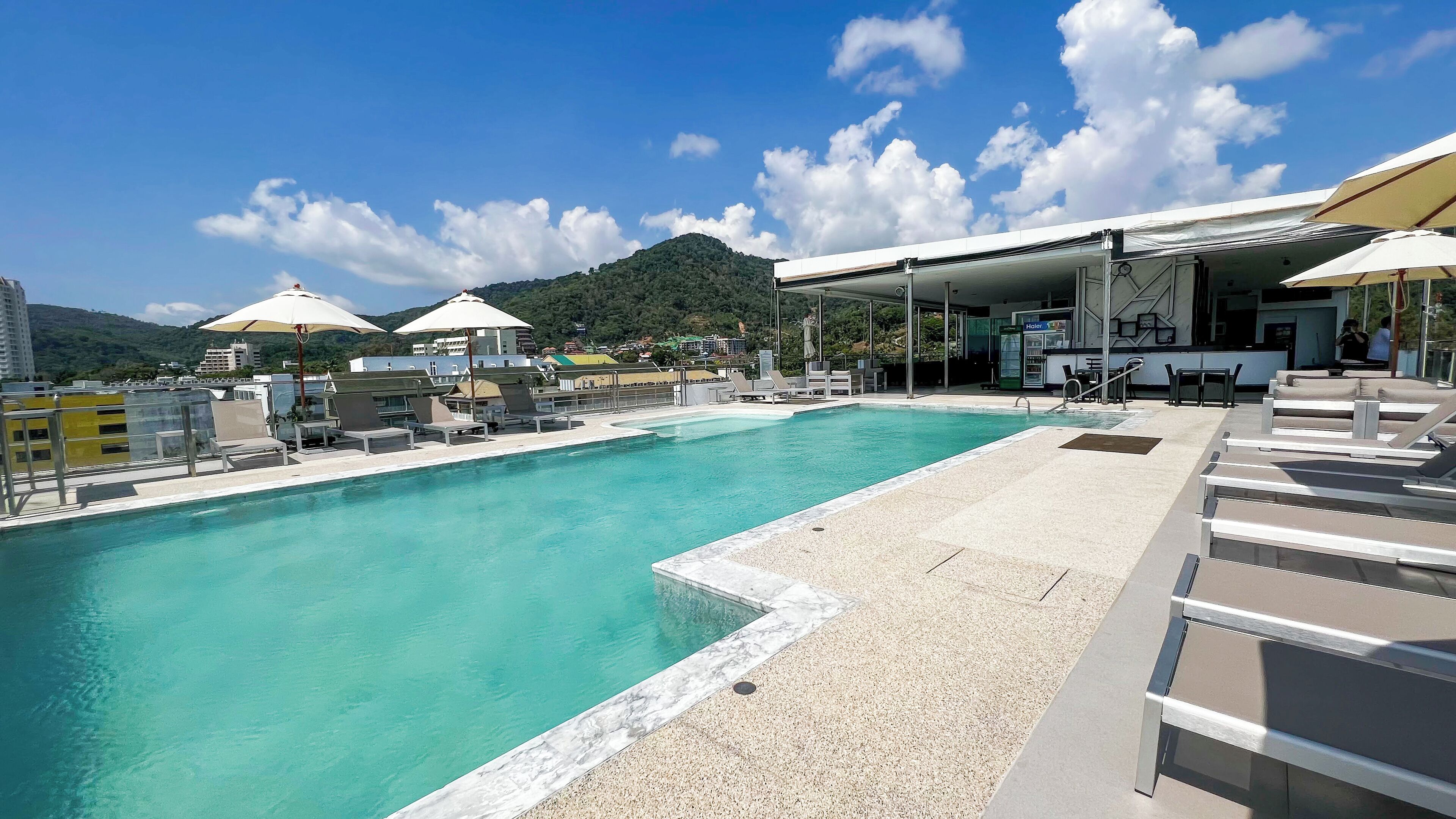 A swimming pool with lounge chairs and umbrellas, a covered seating area, and a view of a mountain in the background.