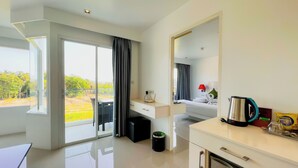 A modern hotel room with a balcony, a kitchenette, and a bed with a red lamp. - Grand Sunset Hotel Phuket (Karon)