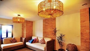 A cozy living room with a brick wall, two sofas, a large woven light fixture, and a potted plant. - Phuket Heritage Hotel (Karon)