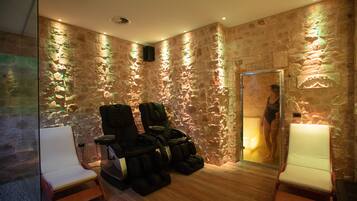 A spa room with stone walls, massage chairs, and a glass door leading to a shower area.