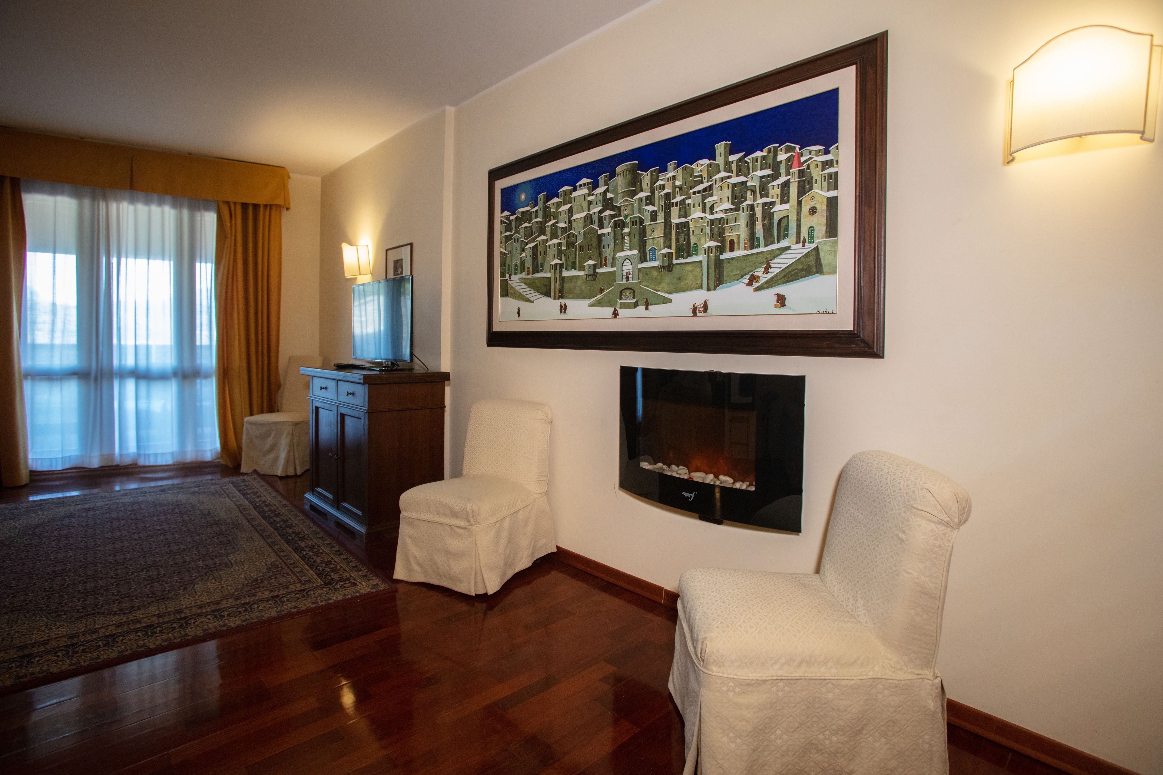 Una sala de estar con chimenea, dos sillones, un televisor y un cuadro enmarcado en la pared.