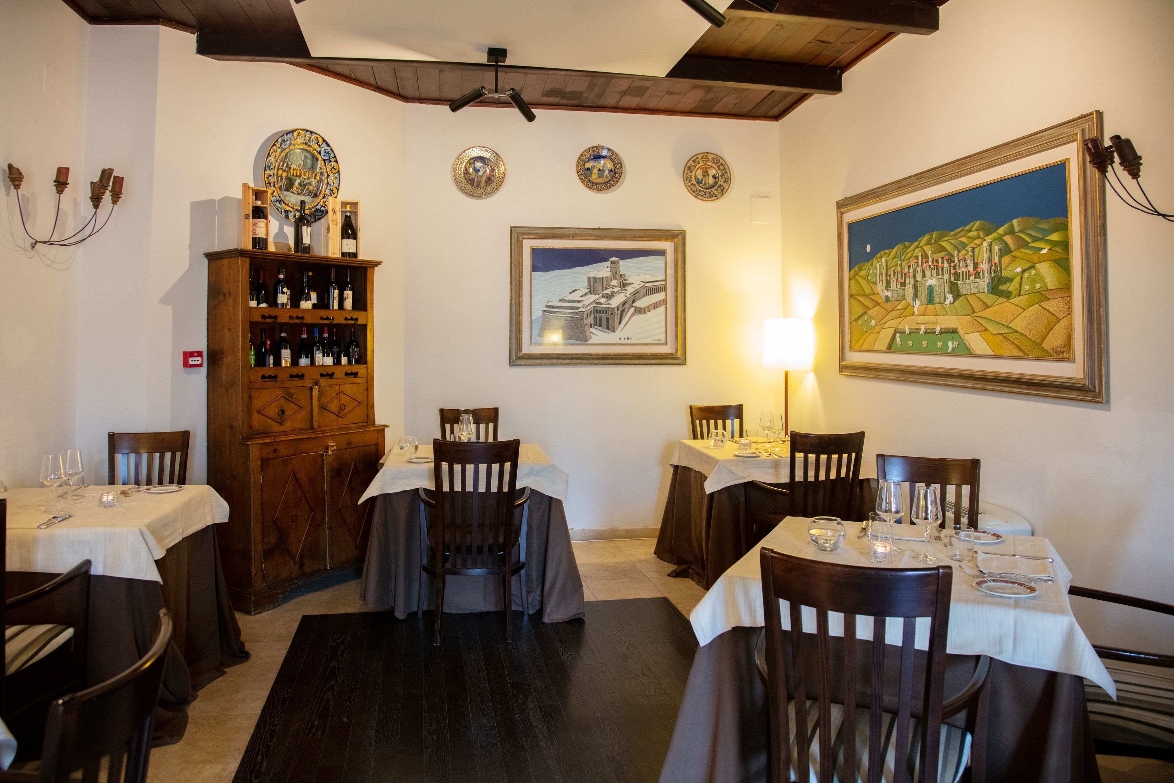 Un coin repas avec des tables préparées pour accueillir quatre personnes, des chaises en bois, un meuble à vin et des assiettes décoratives accrochées au mur.