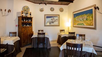 Un coin repas avec des tables préparées pour accueillir quatre personnes, des chaises en bois, un meuble à vin et des assiettes décoratives accrochées au mur.