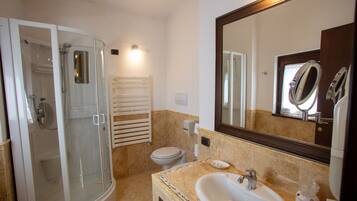 A bathroom with a glass-enclosed shower, a toilet, a sink with a mirror, and a towel rack.