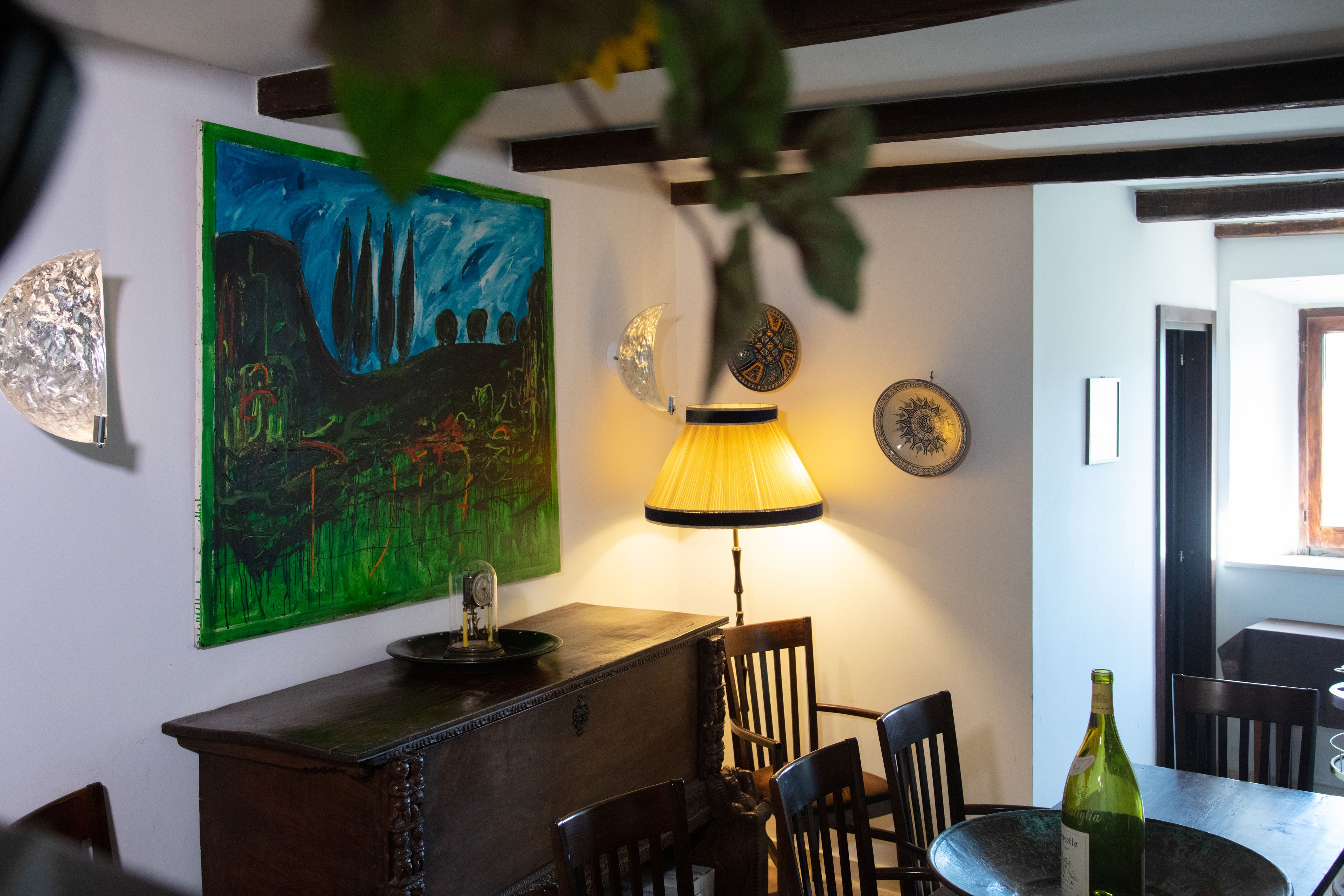 A dining area with a table, chairs, a lamp, and a painting on the wall.