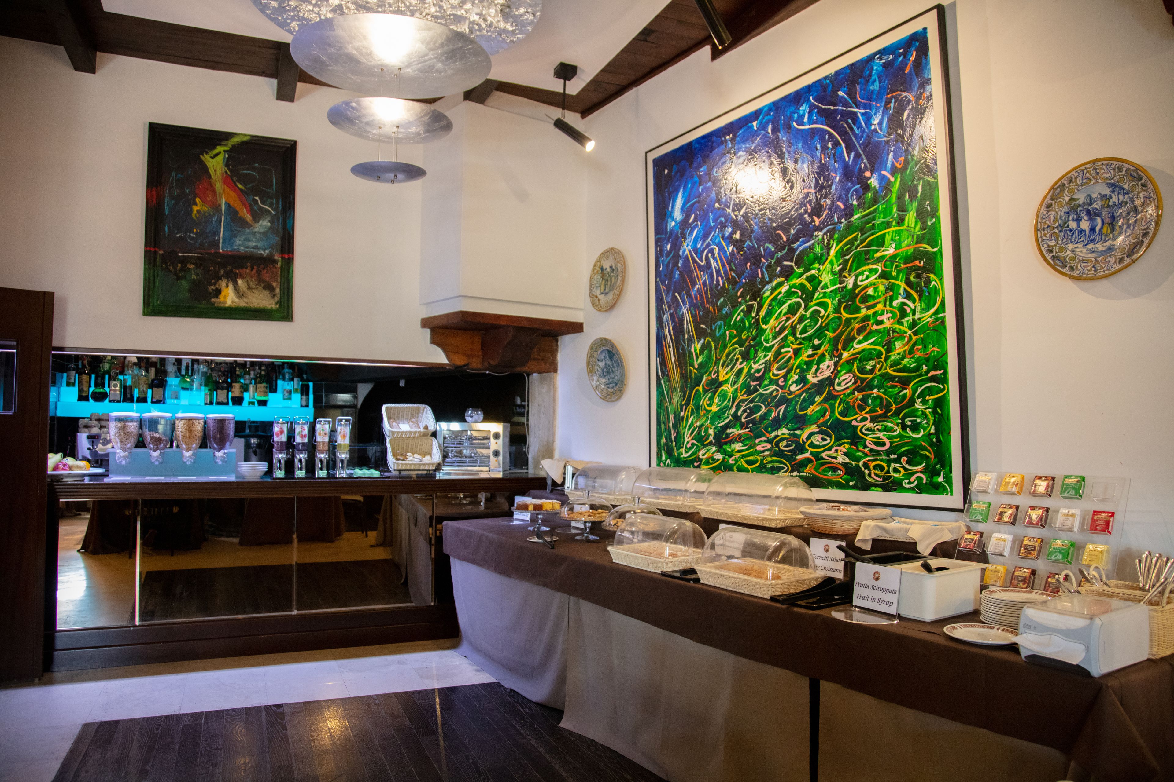 Una zona de bar con mostrador, diferentes opciones de comida y un cuadro abstracto grande en la pared.