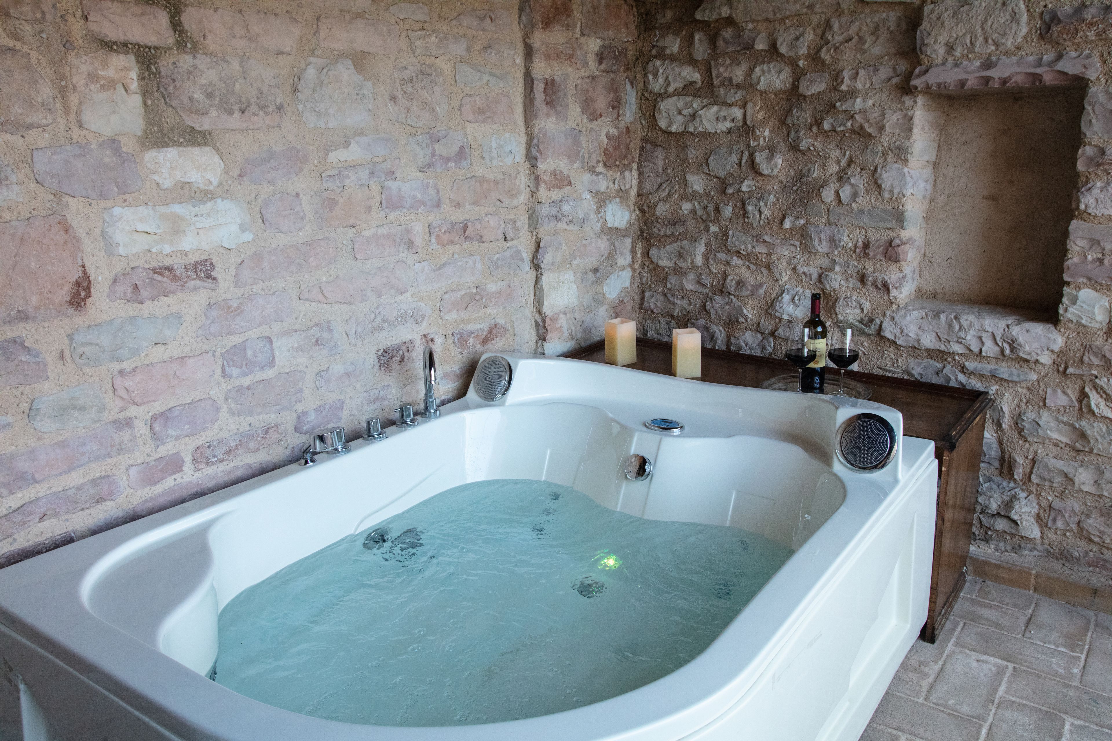 Un bagno con pareti in pietra, una vasca freestanding, candele e una bottiglia di vino.