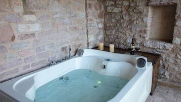 Un bagno con pareti in pietra, una vasca freestanding, candele e una bottiglia di vino.