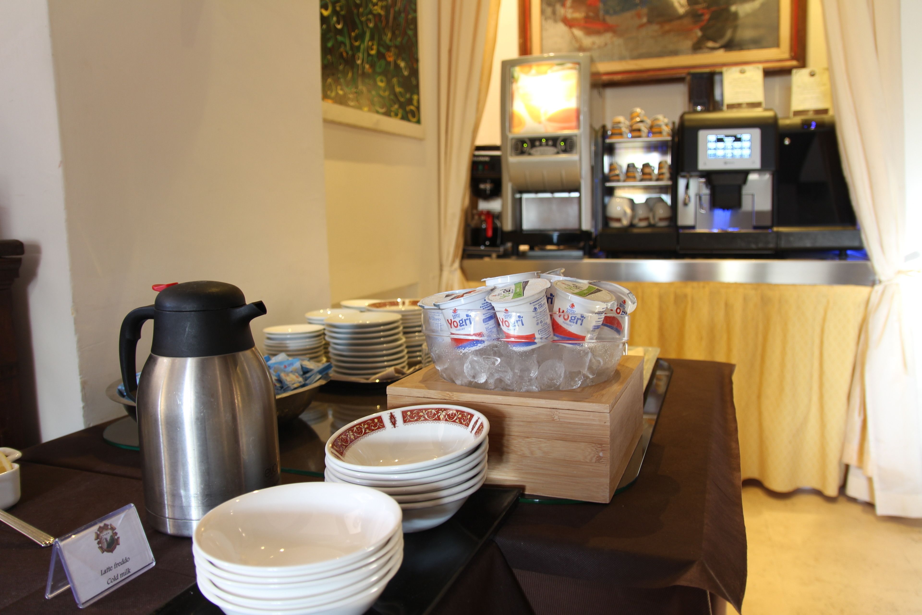Un buffet della colazione con piatti, ciotole, una caffettiera e un frigorifero sullo sfondo.