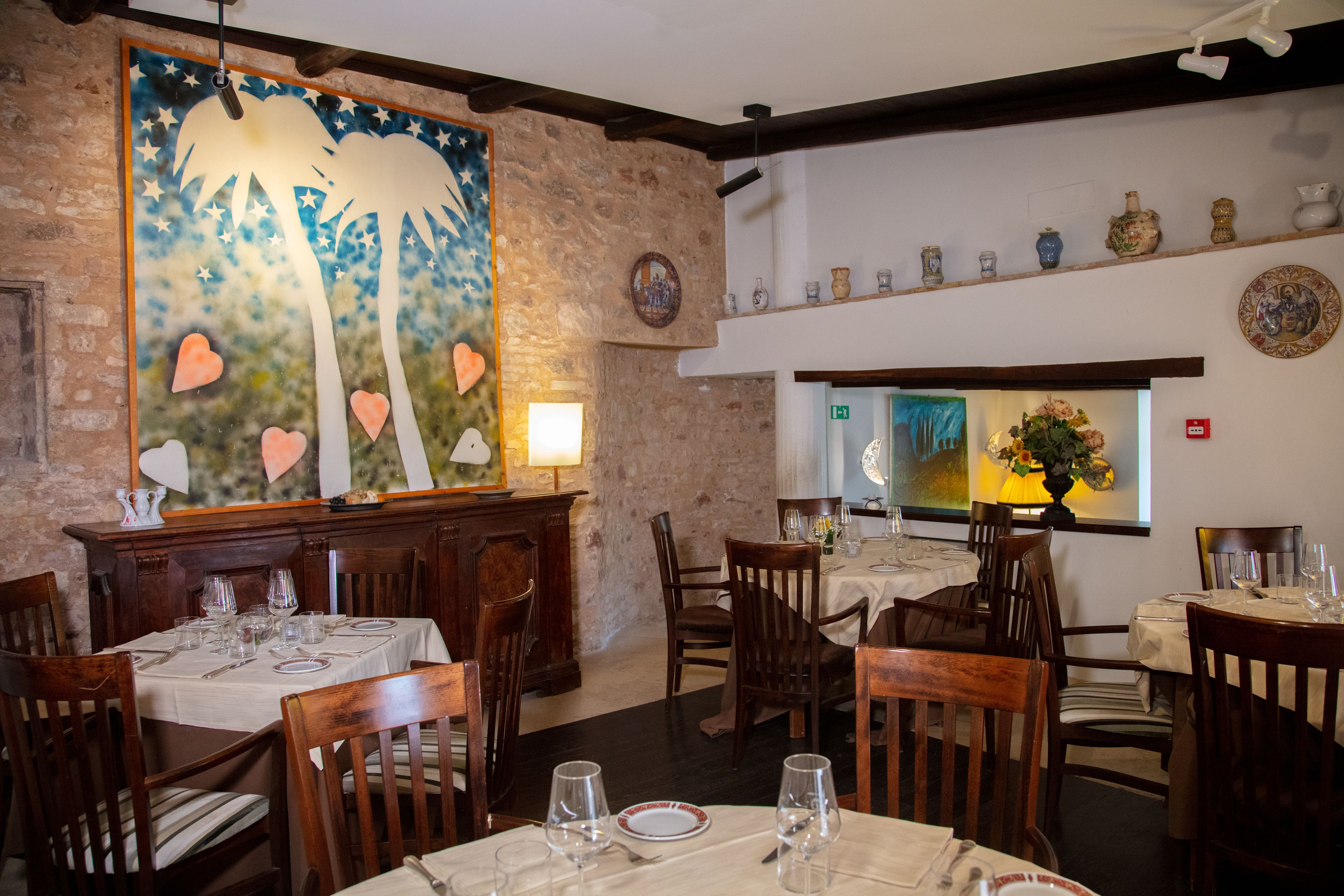 A restaurant with wooden furniture, a large painting on the wall, and a variety of dishes displayed on shelves.