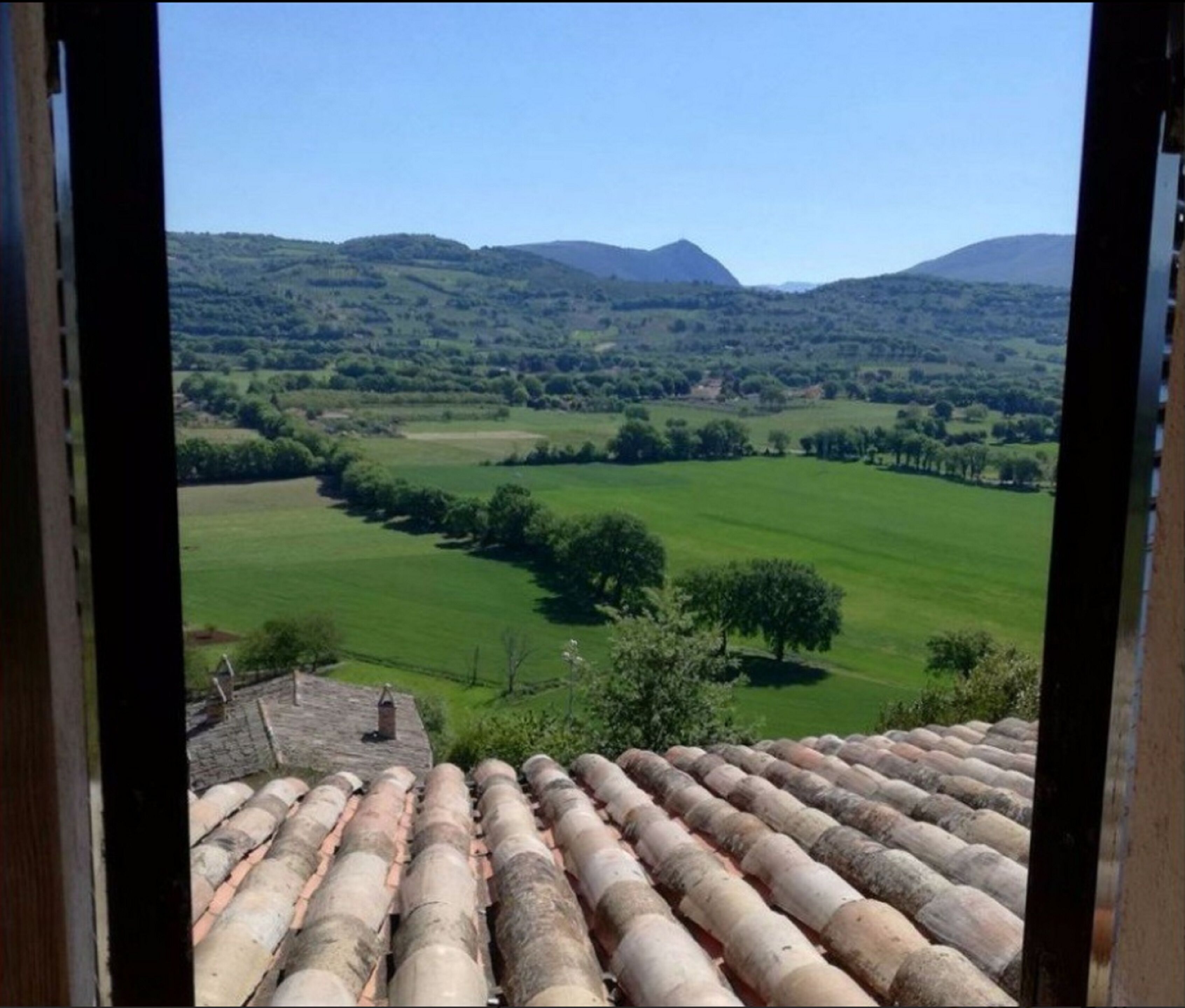A view from a window overlooking a green landscape with rolling hills and a clear sky.