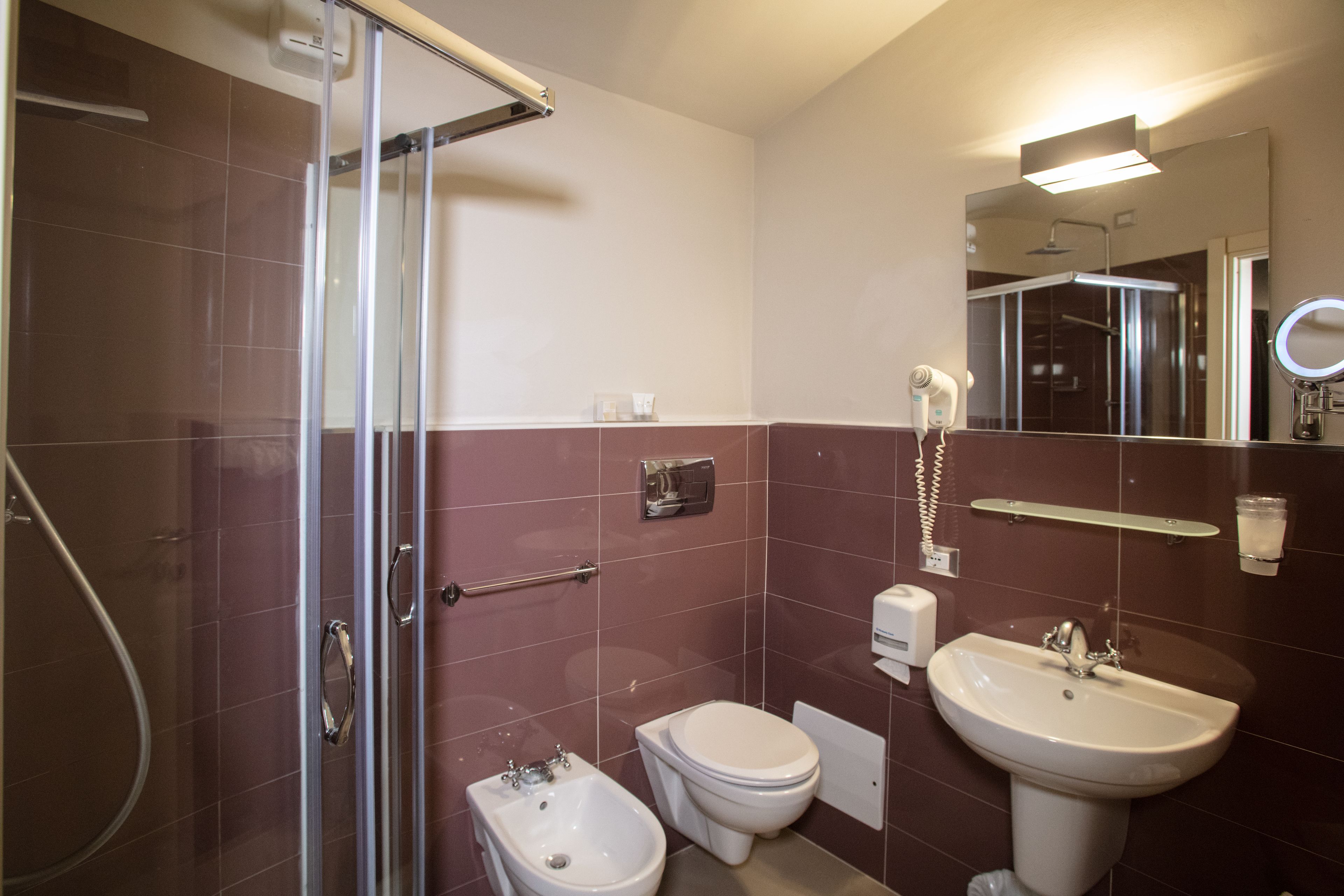 Un baño con cabina de ducha de vidrio, un bidé, un inodoro y un lavabo con espejo.