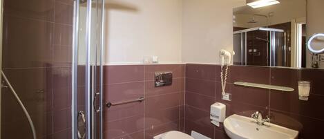 A bathroom with a glass shower enclosure, a bidet, a toilet, and a sink with a mirror above it.