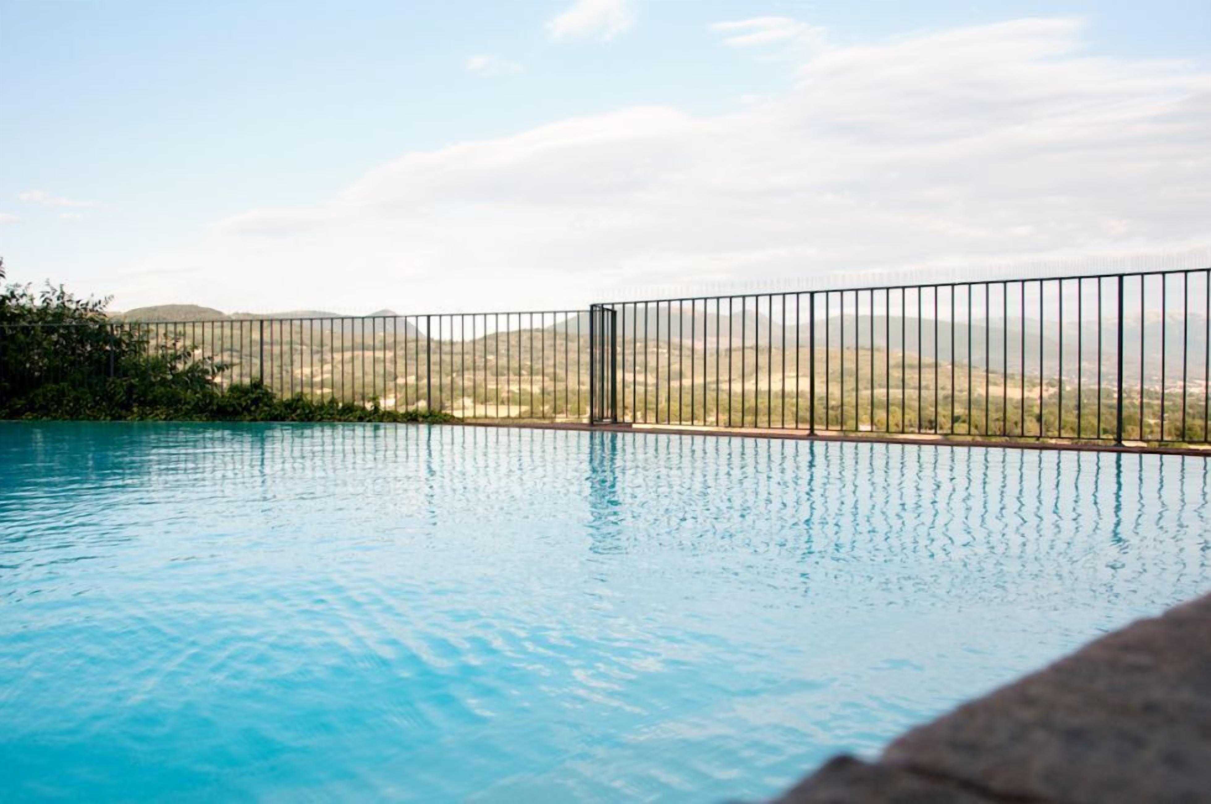 A clear blue pool with a metal fence and a view of distant hills.