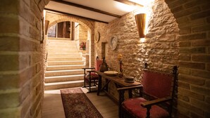 A narrow stone-walled corridor with a wooden staircase leading to an upper level. A table with chairs and a vase of flowers are positioned near the staircase. - Hotel Ristorante La Bastiglia (Spello)