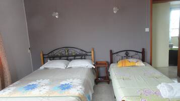 A room with two beds, each with a floral bedspread and a wooden headboard. There is a small wooden nightstand between the beds.