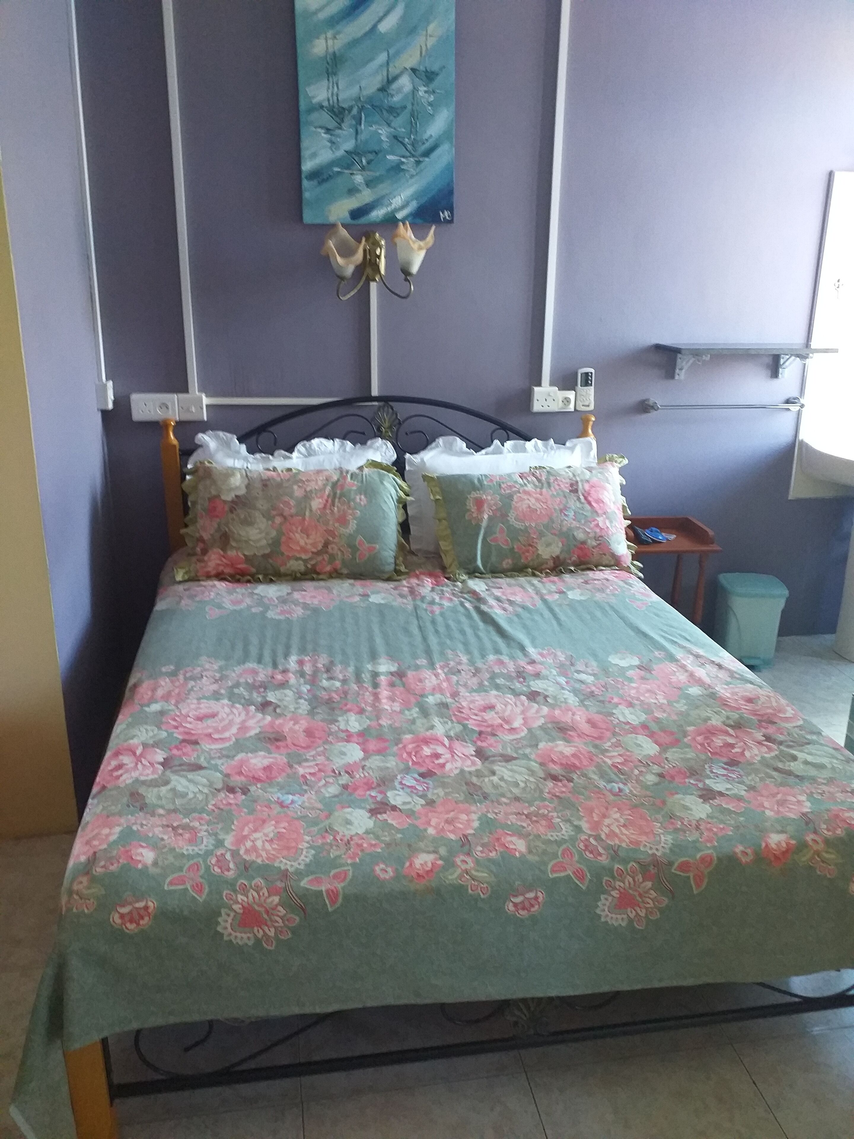 A bedroom with a bed, floral bedding, a wall-mounted light fixture, and a painting.