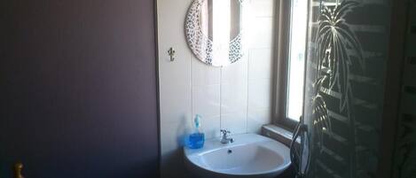 Un baño con un lavamanos blanco, un espejo con diseño de mosaico y una ventana con vista a palmeras.