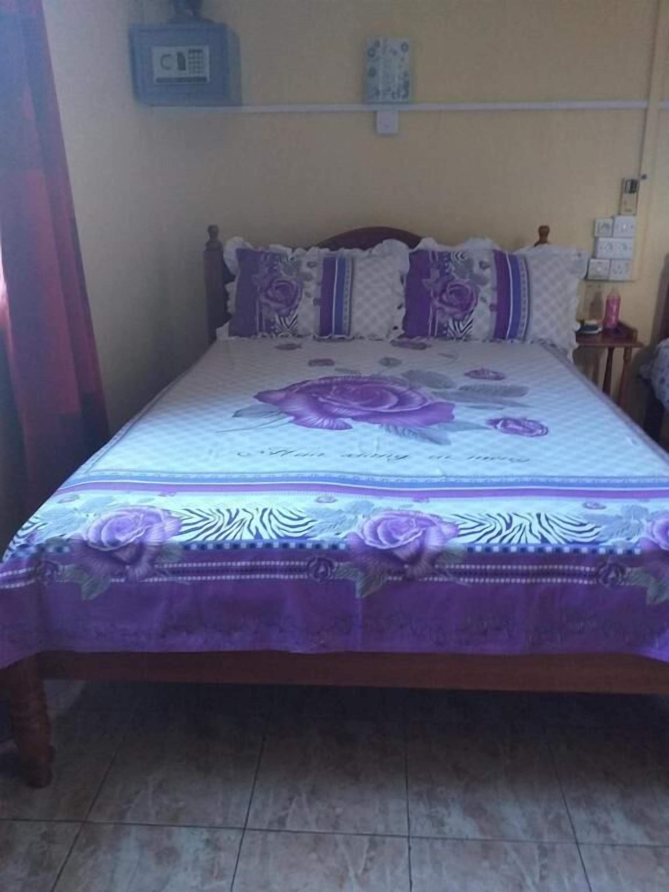 Una cama con una colcha floral púrpura, un cabecero de madera y un teléfono instalado en la pared.