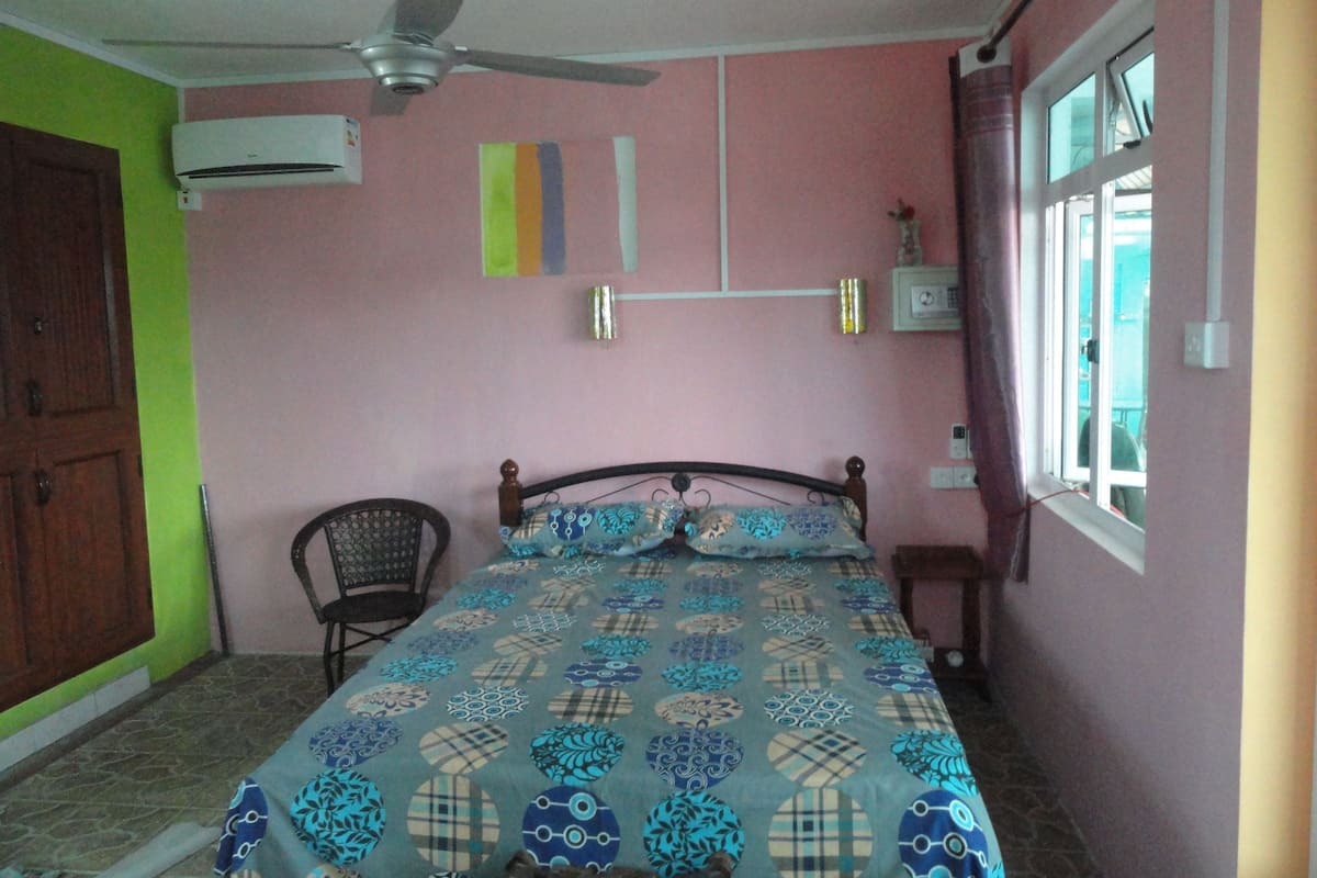 Une chambre à coucher comprenant un lit, une chaise, un ventilateur de plafond, un appareil de climatisation et une fenêtre.
