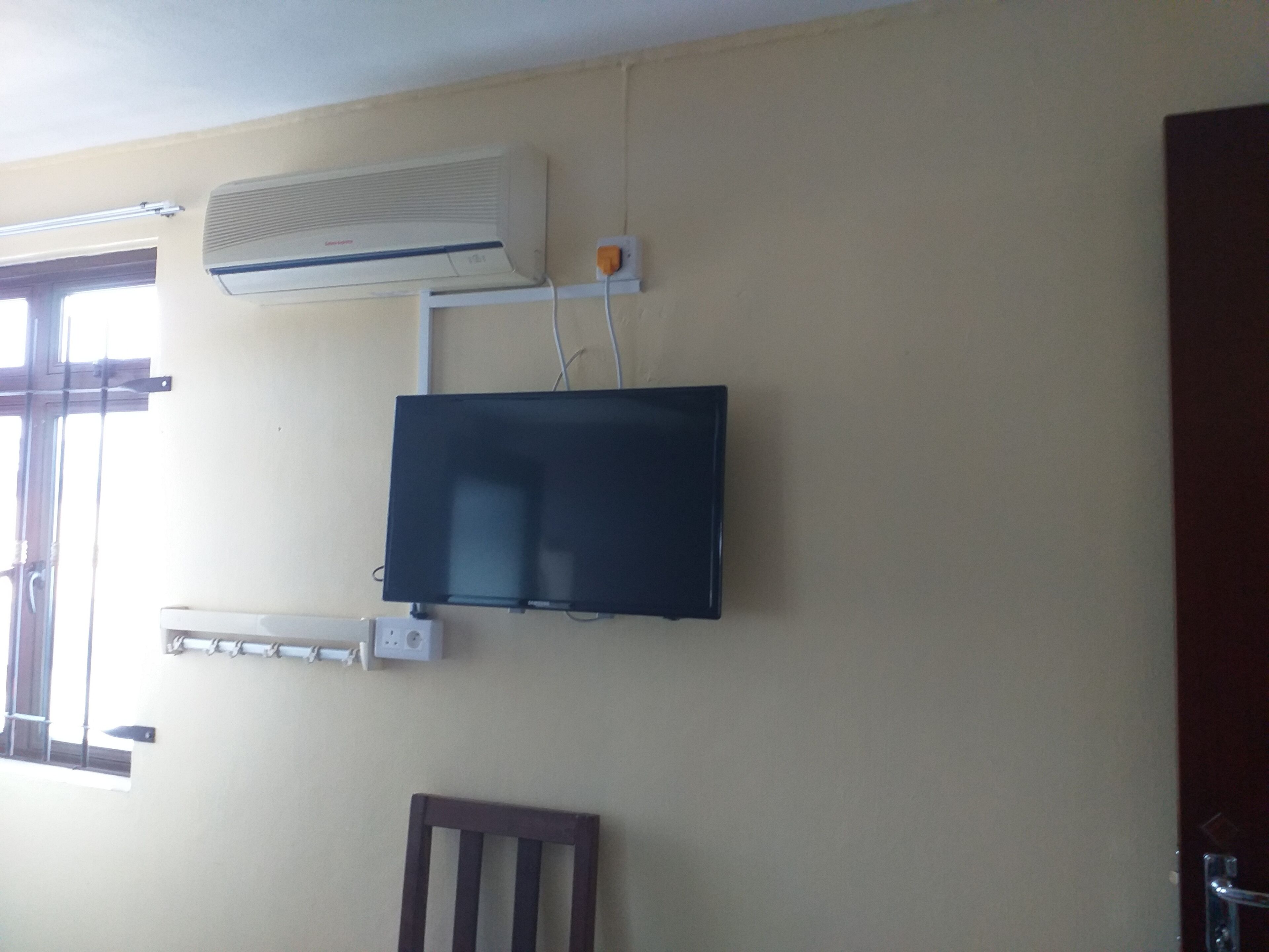 A room with a mounted air conditioner, a television, and a window with blinds.